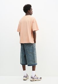 Kortærmet, pastel ferskenfarvet t-shirt parret med løse denimshorts, der har en falmet vask og baglommer. Afsluttet med atletiske sneakers.