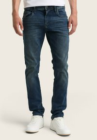 Tmavomodré džíny so slim fit strihom, ktoré maj�ú päť vreciek, jemné vyblednutie a detaily šitia. Nosia sa s bielymi teniskami.