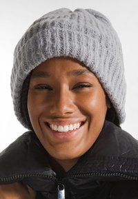 Gorro tejido gris con textura acanalada, diseño ligeramente holgado. Usado sobre una chaqueta negra con cremallera, que presenta un acabado suave.