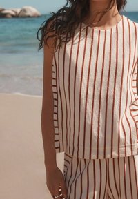 Striped cotton tank top with horizontal red stripes on a cream background, featuring a relaxed fit and minimalistic design, paired with matching shorts.