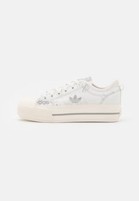 Cream-colored low-top sneaker with thick sole, lace-up front, and subtle printed details on the fabric upper.