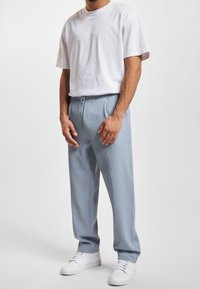 Lichtblauwe, geribbelde joggers met geplooide details en een elastische tailleband, gecombineerd met een eenvoudig wit T-shirt met ronde hals en witte sneakers.