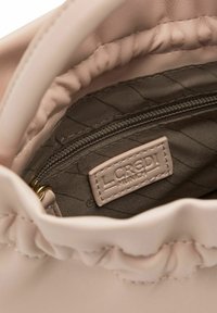 Intérieur d'un sac à main en cuir rose avec doublure matelassée, comportant une poche zippée et une étiquette de marque. Texture douce et bord supérieur froncé.