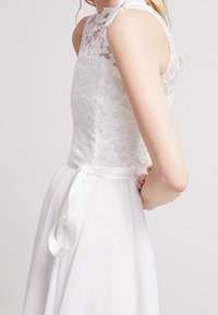 Vit klänning med spetstopp och satinsnöre i midjan. Lång, flödande kjol av slätt tyg. Elegant, figursydd design.