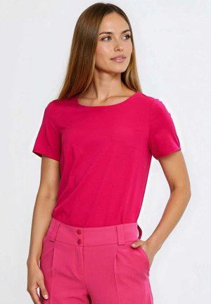Dopasowany top z krótkim rękawem w jaskrawym różowym kolorze, z okrągłym dekoltem. Materiał o fakturze z delikatnym połyskiem, zestawiony z różowymi spodniami z wysokim stanem.