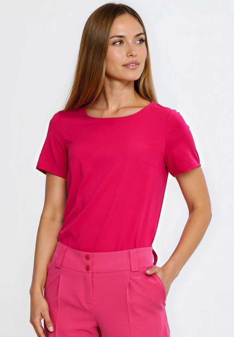 Dopasowany top z krótkim rękawem w jaskrawym różowym kolorze, z okrągłym dekoltem. Materiał o fakturze z delikatnym połyskiem, zestawiony z różowymi spodniami z wysokim stanem.