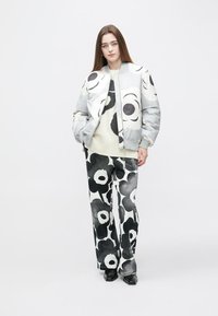 Svetlo sivo bomber jakno z velikimi črnimi cvetličnimi vzorci, kombinirano s črno-belim cvetličnim puloverjem in vzorčastimi hlačami. Črni čevlji.