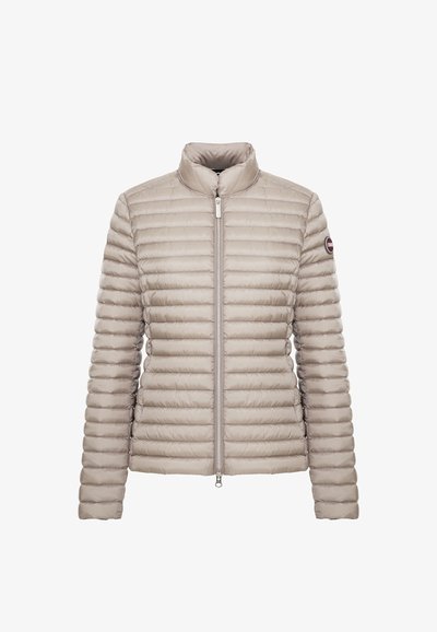 Veste matelassée beige clair avec fermeture éclair intégrale à l'avant et col montant, avec un patch logo rond sur la manche supérieure gauche.
