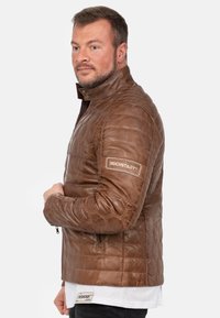 Bruine leren jas met een geborduurd patroon, hoge kraag en ritszakken aan de zijkant. Bevat het 'REICHSTADT' logo op de linkerarm.