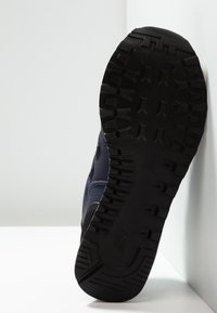 Schwarze Gummisohle mit tiefen Profilen, kombiniert mit einem oberen Teil aus marineblauem Stoff mit strukturierten Akzenten und einem seitlichen logopanel.