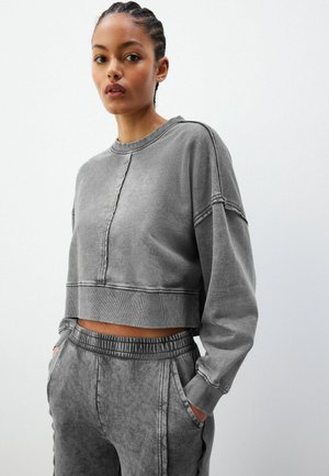 Grijze cropped sweatshirt met een gladde textuur, geribbelde ronde hals en zichtbare stiksels. Gecombineerd met bijpassende grijze sweatpants met koord.