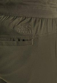 Pantalones verde oliva con textura de espiga, con una cinturilla elástica y un bolsillo trasero. El logo de The North Face está bordado en negro.