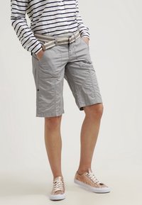 Jasnoszare szorty cargo z bocznymi kieszeniami, pleciony beżowy pasek i casualowa koszula w granatowo-białe paski. W połączeniu z różowo-złotymi sneakersami.