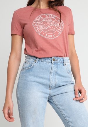Rose-colored t-shirt with a white graphic design reading "CHASING THE LIGHT" and high-waisted blue jeans with a faded texture.