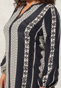 Pitkähihaisessa tummansinissä silkki-paidassa on monimutkaisia kermaisia kuvioita, V-pääntie ja elastiset hihansuut, mikä luo rentoa istuvuutta.