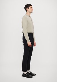 Polo skjorte i lys beige, lange ærmer og afslappet pasform, parret med sorte slim-fit bukser og sorte loafers med grå sokker.