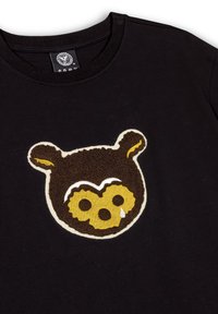 Camiseta negra con un aplique de cara de oso marrón y amarillo con acentos texturizados. Diseño de cuello redondo y mangas cortas.