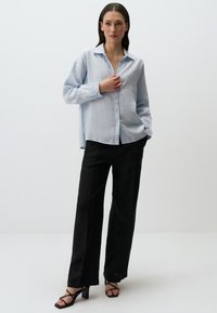 Lichtblauw overhemd met een relaxte pasvorm en lange mouwen, gecombineerd met zwarte wijde broek en zwarte schoenen met bandjes.