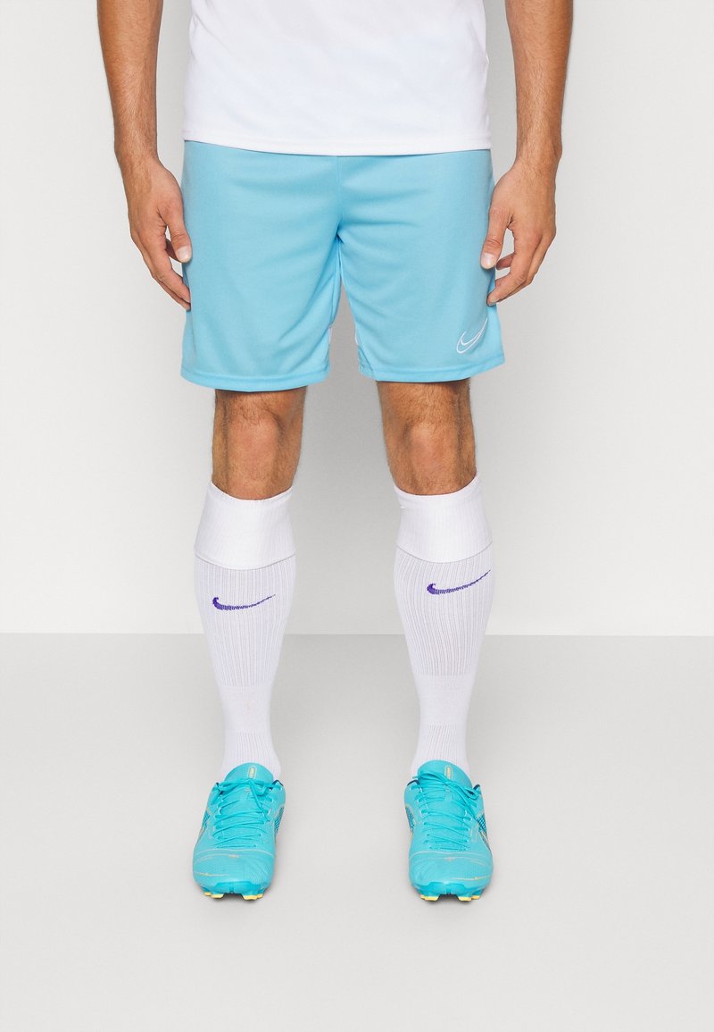 Světle modré sportovní kraťasy s bílým logem Nike, spárované s bílými ponožkami po kolena s fialovými akcenty a jasně modrými fotbalovými kopačkami.