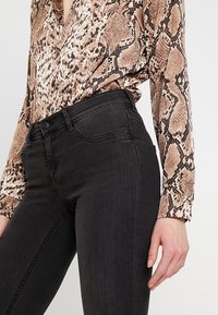 Jean noir à coupe ajustée avec des coutures discrètes, associé à un blouse à imprimé serpent dans des tons de brun et beige.