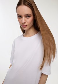 T-shirt in cotone bianco con scollo rotondo classico, maniche corte e vestibilità rilassata, mostrato con una texture liscia e design minimalista.