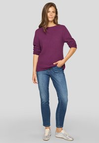 Lila strukturierter Pullover mit langen Ärmeln, kombiniert mit blauen Jeans und silbernen Sneakers, bietet einen lässigen Schnitt und ein einfaches Design.