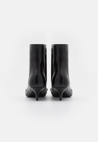 Musta nahkainen nilkkuri, jossa on tyylikäs muotoilu, teräväkärkinen ja 5 cm:n stiletto-korko. Takana on vetoketju. Suora pinta.