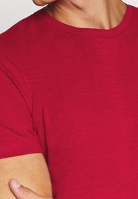 T-shirt rosso a maniche corte caratterizzato da una texture liscia, colletto rotondo classico e un sottile motivo melangiato. Tessuto leggero con vestibilità standard.