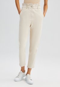 Beiga tapered byxor med hög midja och rynkade detaljer, med sidofickor och bärs med vita sneakers. Slät textur, avslappnad stil.