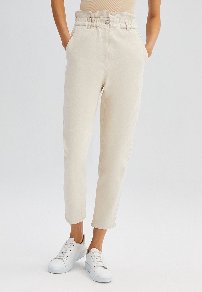 Beiga tapered byxor med hög midja och rynkade detaljer, med sidofickor och bärs med vita sneakers. Slät textur, avslappnad stil.