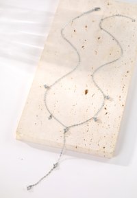 Collier en chaîne d'argent avec des gemmes claires dispersées, présentant un design en forme de Y avec un pendentif plus long au centre, posé sur une surface texturée.