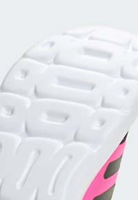 La semelle de la chaussure présente une surface texturée blanche avec des rainures profondes, ainsi qu'une partie supérieure rose et noire avec des accents gris.