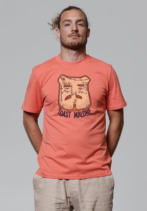 Korallfarbenes T-Shirt mit kurzen Ärmeln, das ein grafisches Design eines gerösteten Brotscheibes mit dem Text "TOAST MALONE" zeigt, aus Baumwolle. Glatte Textur.