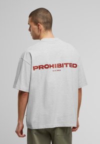 Tricou supradimensionat de culoare gri deschis, cu mâneci scurte, care are un text roșu îndrăzneț "PROHIBIT" pe spate, cu "10119, BERLIN" dedesubt. Textură moale.