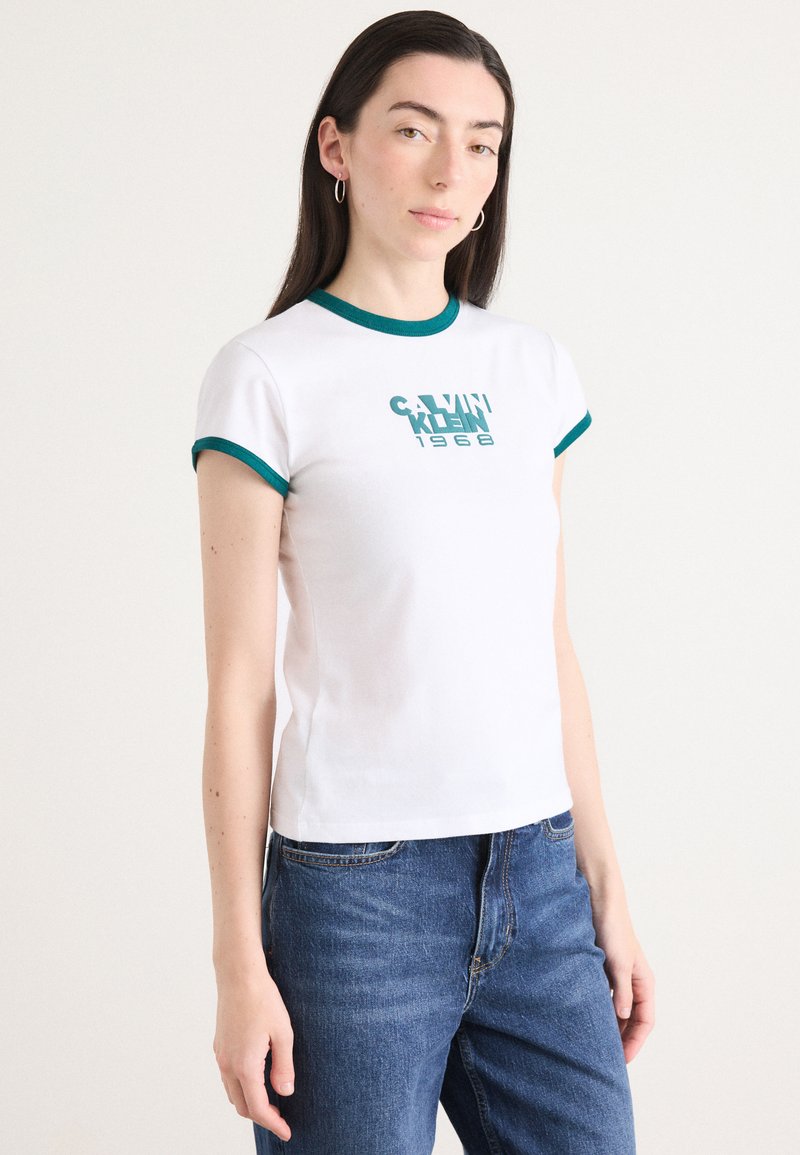 White cotton t-shirt with green trim on sleeves and neckline; features "CALVIN KLEIN 1968" graphic in teal. Soft texture, fitted design.