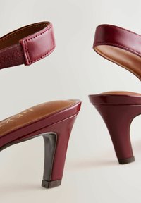 Burgunderfarbene High Heels Sandalen mit einer glatten Lederoberfläche, weichen braunen Innensohlen und einem kontrastierenden schwarzen Absatz. Verstellbare Riemen.