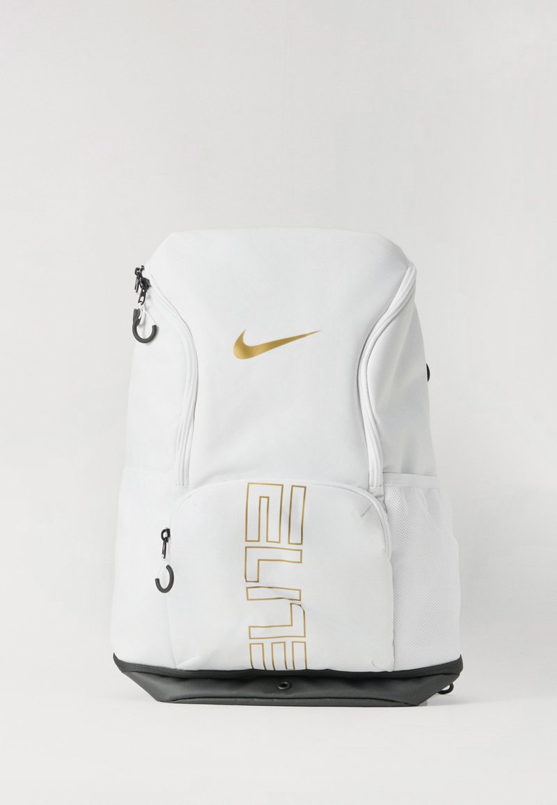 Biely batoh Nike so zlatým logom, má zipsové priehradky, čierne dno a sieťované bočné vrecká. Jednoduchý dizajn, funkčné detaily.