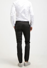 Svarta skräddarsydda byxor i vävd tyg med smal passform och rena linjer, kombinerade med vit skjorta och grå sneakers.