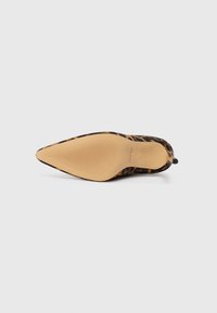 Puntige schoen met luipaardprint, met een zwarte stoffen bovenkant, een gladde beige zool en textuurpatronen op de zool voor grip.