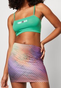 Grön crop top med tunna band och broderad logo, ihopparad med en färgglad figurnära minikjol med ett cirkulärt mönster i lila och orange.