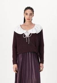 Temno burgundska pulover s velikim belim ovratnikom, ki ima zavezovanje ob vratu. Obut s plišasto vijolično krilom.
