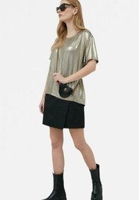 Top corto metallico oro abbinato a una mini gonna nera. L'outfit è completato con stivaletti neri e una piccola borsa a mano nera.