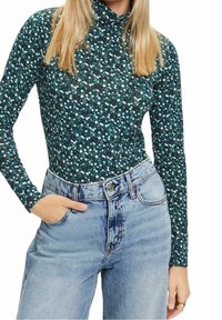 Body a maniche lunghe di colore teal con un motivo floreale bianco e azzurro chiaro, abbinato a jeans in denim azzurro chiaro a vita alta.