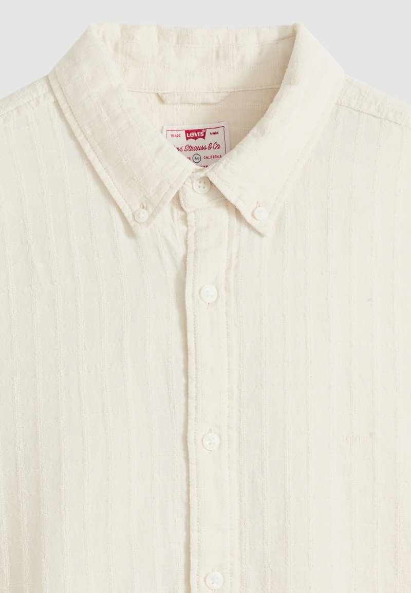 Chemise écrue texturée avec boutons, col à rabat boutonné et étiquette Levi's visible à l'intérieur du col.