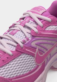 Rožinės ir baltos spalvos Nike bėgimo bateliai su tinklelio intarpais, paminkštintu liežuviu, baltais raišteliais ir matomu Nike logotipu šone.