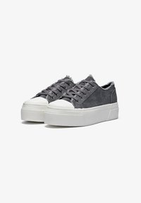Graue Canvas-Sneaker mit strukturiertem Finish, weißer Gummisohle und fransigen Kanten. Sechs Ösen und flache Schnürsenkel runden das Design ab.