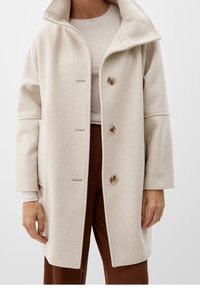 Béžový kabát z vlněné směsi s vysokým límcem, se čtyřmi knoflíky a bočními kapsami. Hladká textura, uvolněný střih a jemný vzor herringbone.