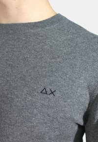 Maglione grigio a maglia con colletto a girocollo a coste. Presenta un logo ricamato di colore blu scuro sul lato sinistro. Texture morbida, design aderente.