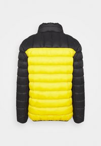 Veste matelassée noire et jaune avec quilting horizontal, vue de dos, avec manches noires et haut du dos avec panneau central jaune.
