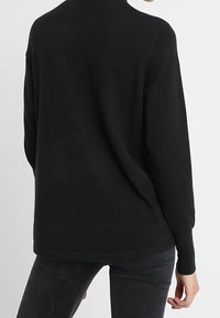 Pull noir à manches longues avec une coupe décontractée, encolure arrondie et ourlet et poignets côtelés. Texture tricotée, fabriqué à partir d'un tissu doux.